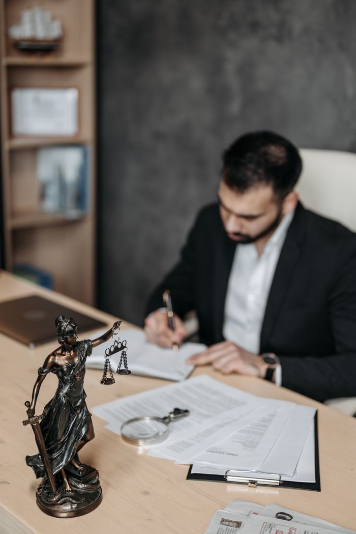 A lawyer concentrates on paperwork in an office; legal statue visible on desk.